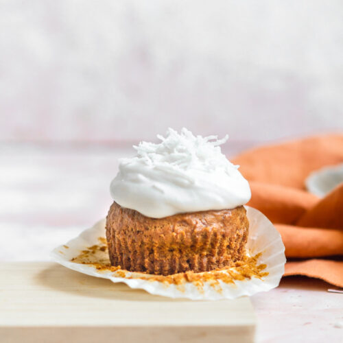 a carrot cake muffin topped with coconut frosting and coconut shreds