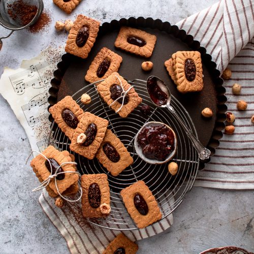 Gingerbread linzer cookies cooling on a rack and being filled