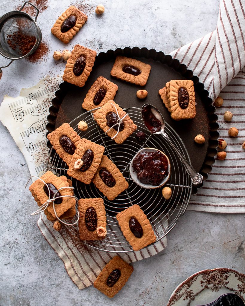 Gingerbread linzer cookies cooling on a rack and being filled