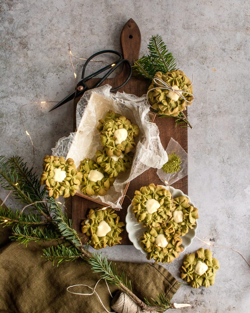 A dark wooden cutting board with tree branches, and a wood box filled with matcha white chocolate cookies.