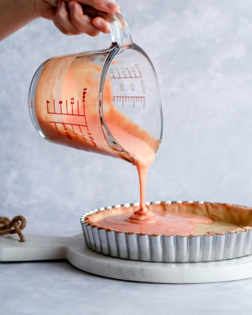 pouring orange curd into a baked tart