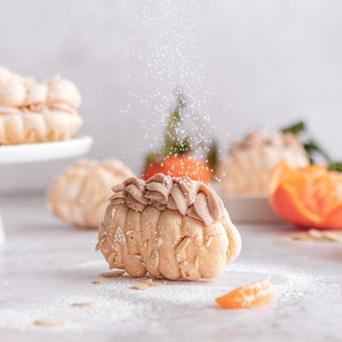 powdered sugar being dusted over a clementine mocha meringue sandwich cookie