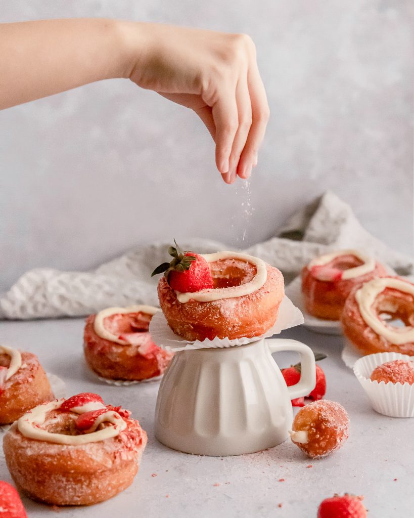 sprinkling sugar on top of a strawberry vanilla bean cronut