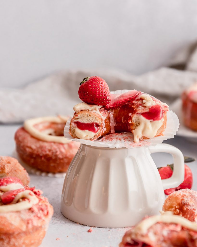 Half a donut resting on a cup with strawberry jam and vanilla bean filling