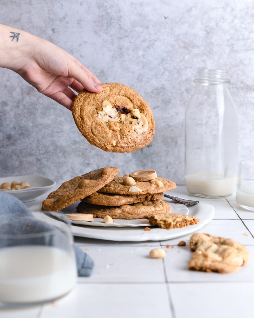 grabbing a carmelized white chocolate macadamia nut cookie from a stack