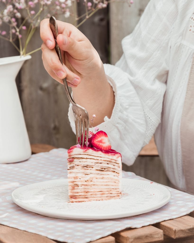cutting into a slice of strawberry vanilla crepe cake