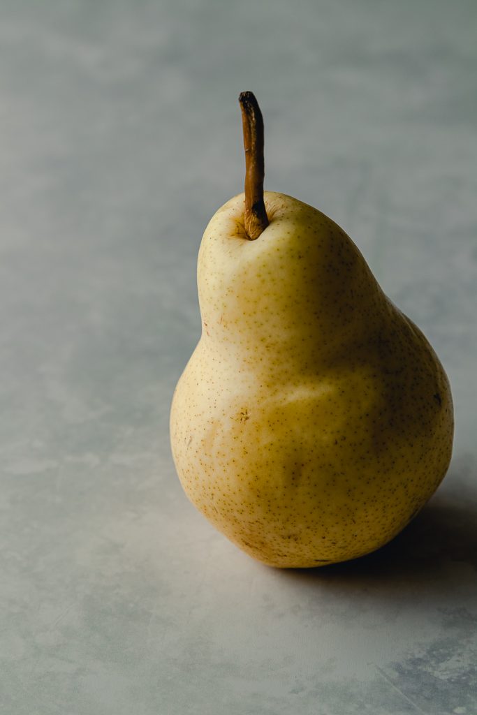 A still life image of a pear being taken with flash photography on a grey blue backdrop. 